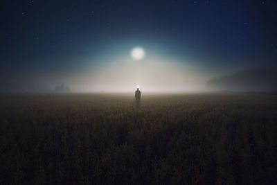 Person standing on field against sky at night during foggy weather