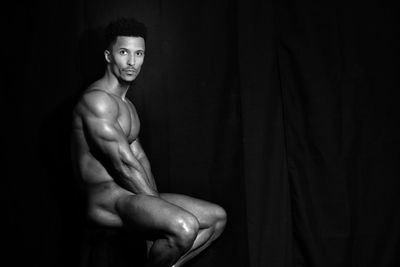 Portrait of shirtless man standing against black background