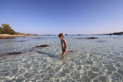 Rear view of woman walking at beach against clear sky