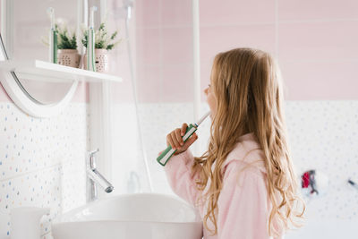 Cute child girl in a pink terry dressing gown brushes her teeth in front of the bathroom mirror 