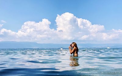 Side view of shirtless woman standing in sea against sky