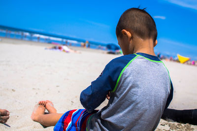 Rear view of boy at beach against sky