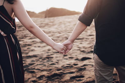Midsection of couple holding hands standing at beach
