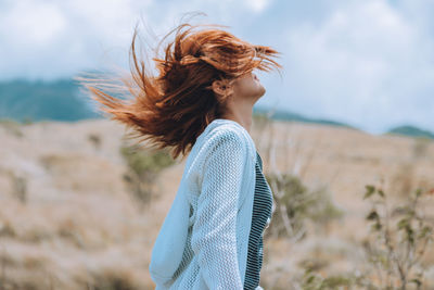 Side view of woman tossing hair against sky