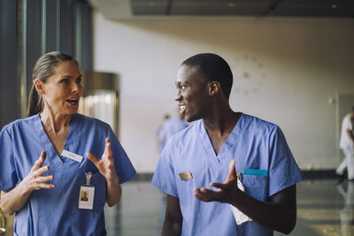 Male and female doctors in blue scrubs discussing while walking at hospital
