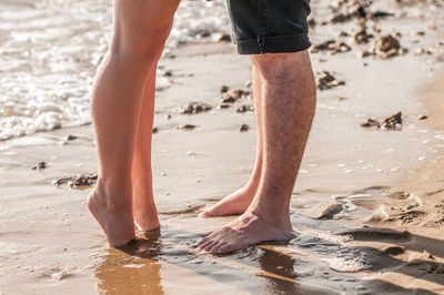 Low section of couple standing on shore at beach