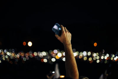 Midsection of person holding smart phone at night