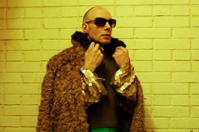 Man wearing sunglasses and fur coat while standing against yellow wall