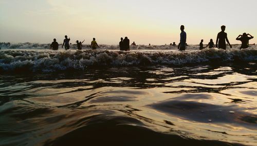 Silhouette people on beach against sky during sunset