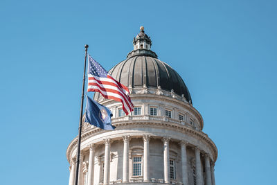 American flag waving at state capitol building with blue sky in background