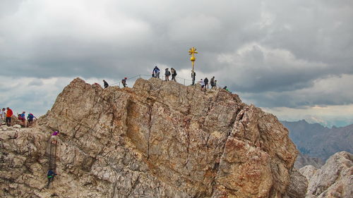 People on rock by mountain against sky