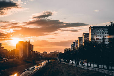 Road by buildings against sky during sunset