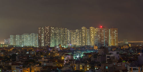 Illuminated modern buildings in city against sky at night