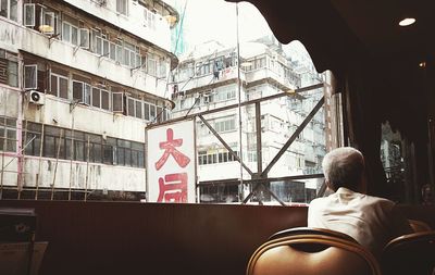 A man in a local cafe with view of hong kong packed apartments.