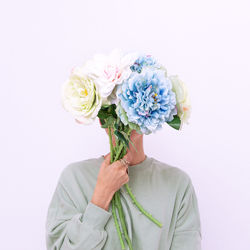 Woman holding flowers in front of face against white background