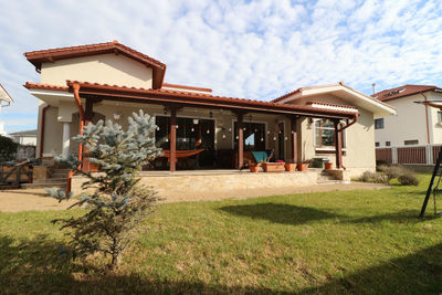 House on lawn by building against sky