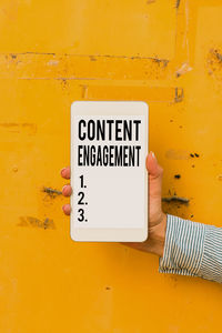 Close-up of hand holding text on yellow wall