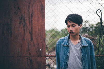 Young man standing against chainlink fence