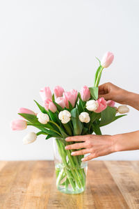 Female's hands put a bouquet of delicate pink and white tulips into a vase.