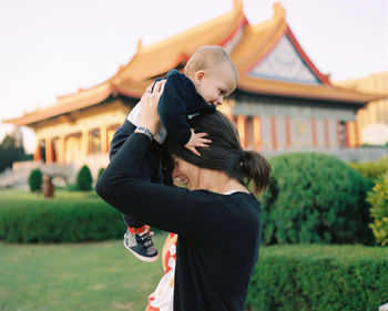 Side view of mother holding son while standing on field