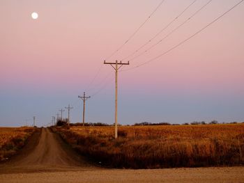 Dirt road amidst grassy landscape against sky during sunset