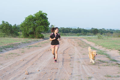 Smiling woman running with dog on dirt road