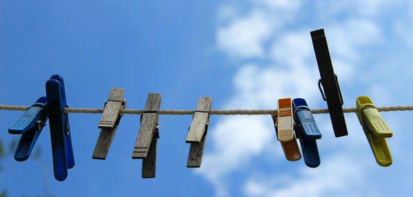 Low angle view of clothespins hanging on rope against sky