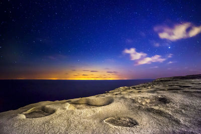 Scenic view of sea and rocky shore against sky at dusk