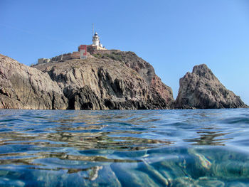 Rock formations by sea against clear blue sky