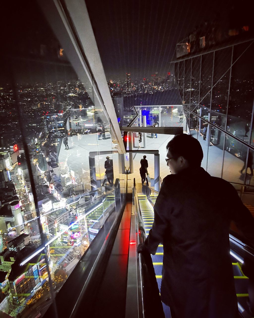 REAR VIEW OF MAN STANDING ON ILLUMINATED RAILROAD STATION