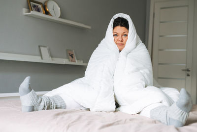 Young adult unhappy lonely woman plus size body positive in white big blanket on bed at home