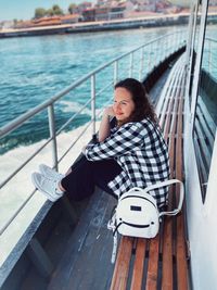 Young woman sitting on railing by boat