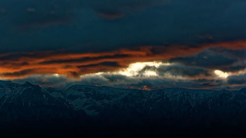 Scenic view of snowcapped mountains against dramatic sky during sunset