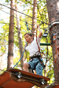 Low angle view of boy on obstacle course in forest