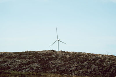 Low angle view of wind turbines on hill against sky
