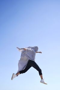Low angle view of man covered with textile jumping against clear blue sky