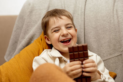 Little adorable boy sitting on the couch at home and eating chocolate bar. child and sweets