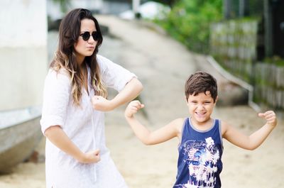 Happy mother with son flexing muscles while standing on street