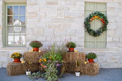 Fall harvest porch decor with colorful mums stacked on hay bales. an autumn wreath hung on a window.