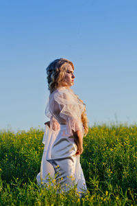 Side view of bride standing on grassy field against blue sky