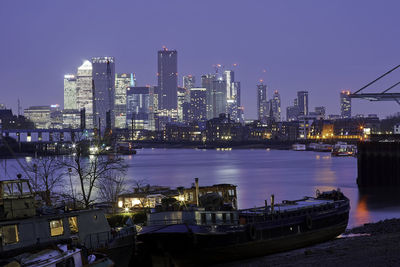 Illuminated buildings by river against sky at dusk