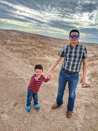 Full length of father and son standing on beach against sky