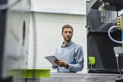 Businessman in high tech company controlling manufacturing machines, using digital tablet