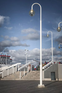 Street lights on pier by city against sky