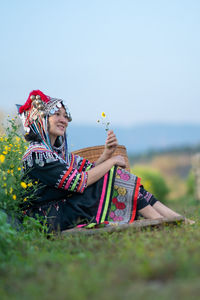 Woman holding umbrella while sitting on field against sky