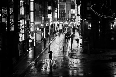 People walking on wet street amidst buildings in city