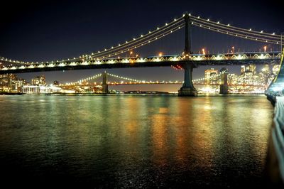 Illuminated bridge over river against sky at night