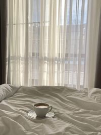 Coffee cup on bed against window at home