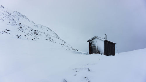 Hut on snow covered mountain against sky