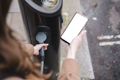 Businesswoman with smart phone holding electric plug at charging station
